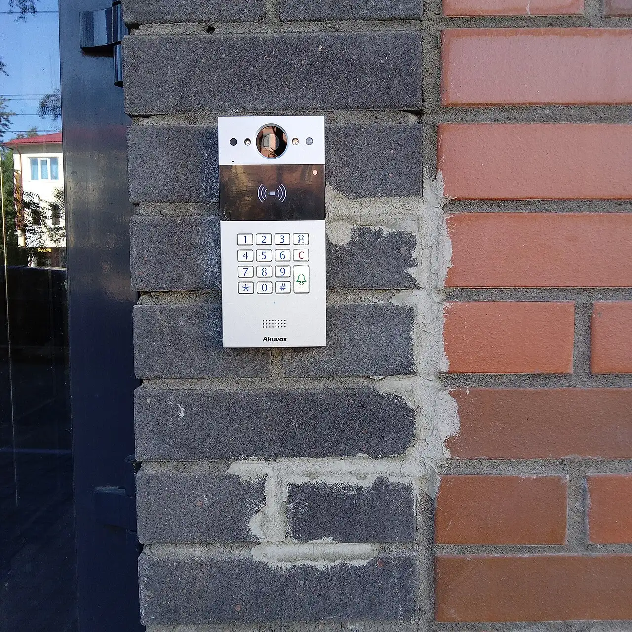 Video door phone entry panel with camera and keypad mounted on a brick wall